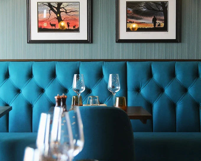 Teal tufted booth seating with framed landscape prints on the wall above