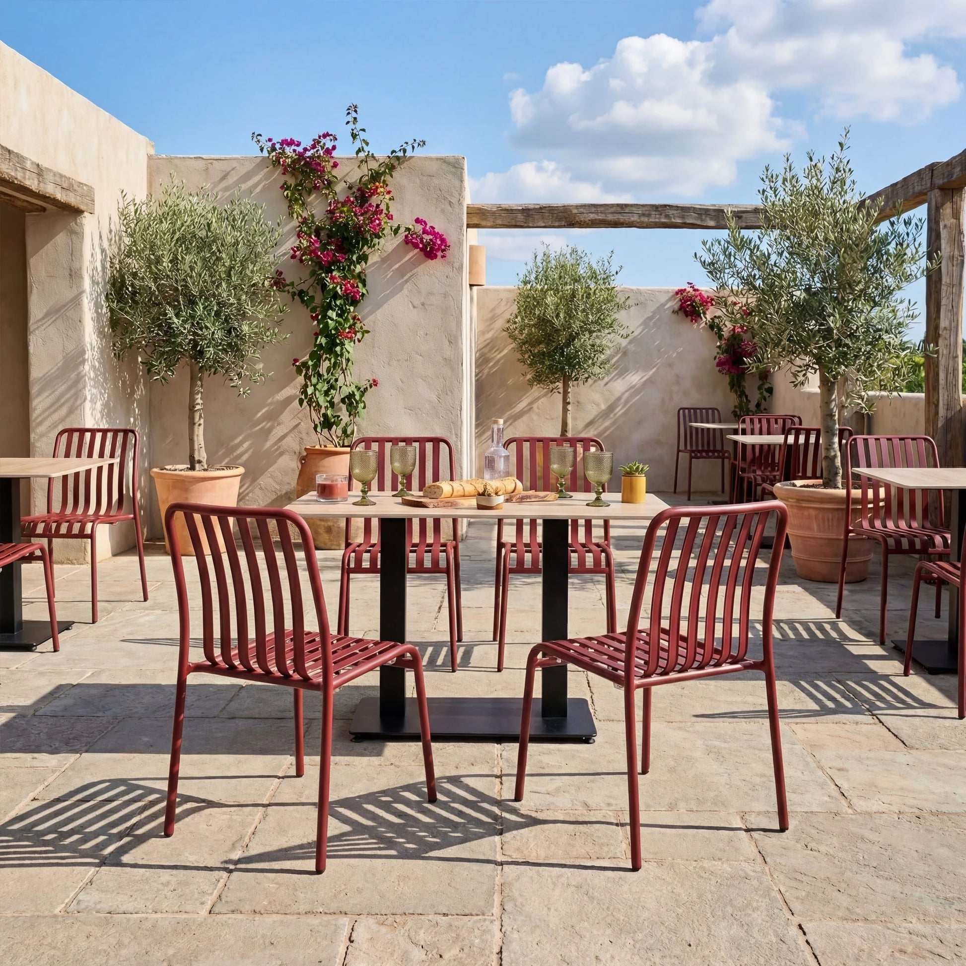 Outdoor seating area with red chairs and tables on a sunny day. Commercial Henley Side Chair in Pine Green featuring a lightweight powder-coated aluminium frame, ergonomic slatted design and stackable construction for hospitality, restaurant, hotel, café and outdoor seating applications.