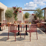 Outdoor seating area with red chairs and tables on a sunny day. Henley Side Chair in Brick Red featuring a contemporary slatted aluminium design with powder-coated finish, suitable for indoor and outdoor hospitality environments.