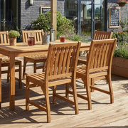 Wooden outdoor dining set on a deck with plants and a garden view.