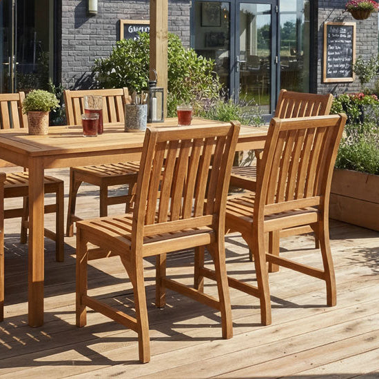 Wooden outdoor dining set on a deck with plants and a garden view.