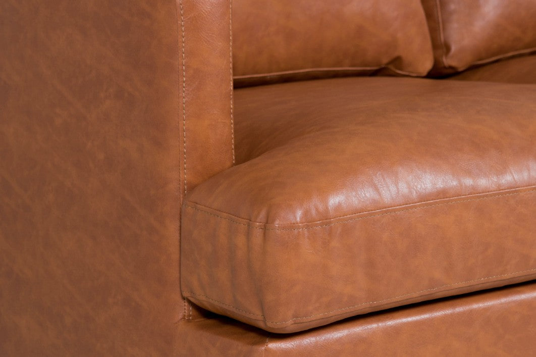 Close-up of a brown leather sofa  Three-seat tan upholstered sofa with padded cushions and slim black metal legs, designed for commercial hospitality and workplace interiors.