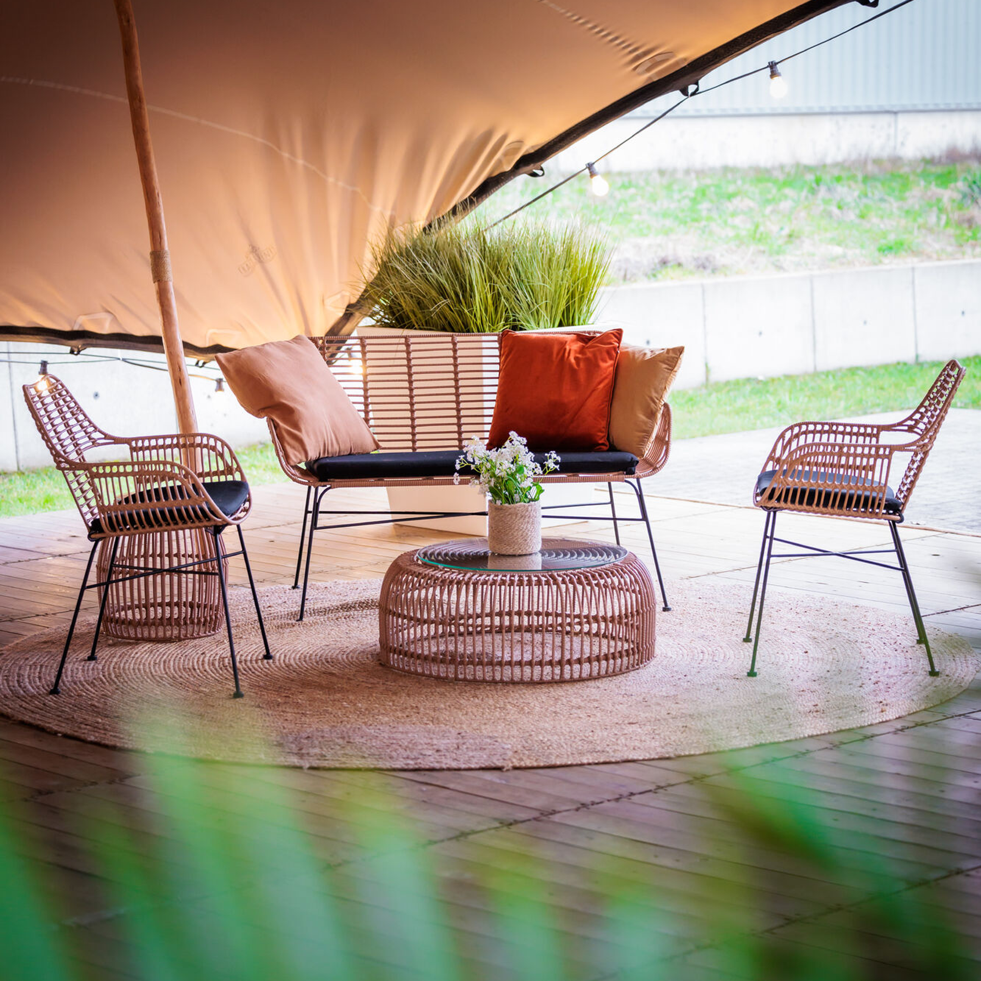 Palm Stacking Sofa in Natural finish featuring woven rattan-style seating and backrest with a black galvanised steel frame, suitable for commercial indoor and outdoor hospitality spaces Outdoor seating area featuring woven chairs and a loveseat with cushions surrounding the Palm Stacking Coffee Table - Natural on a circular rug under a canopy. 