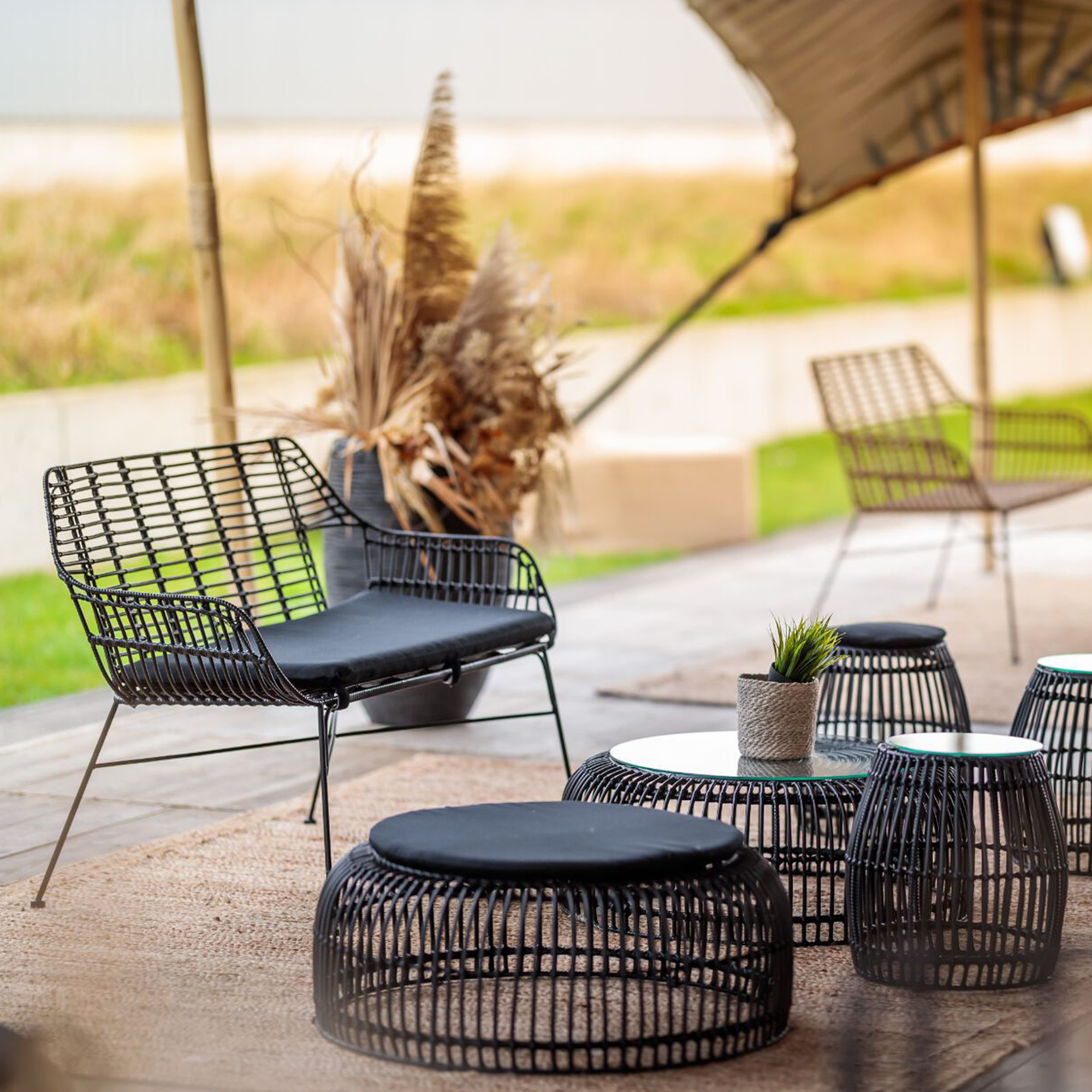 Outdoor seating area featuring the Palm Stacking Coffee Table - Black surrounded by matching black wireframe chairs and ottomans, styled with natural decor accents.