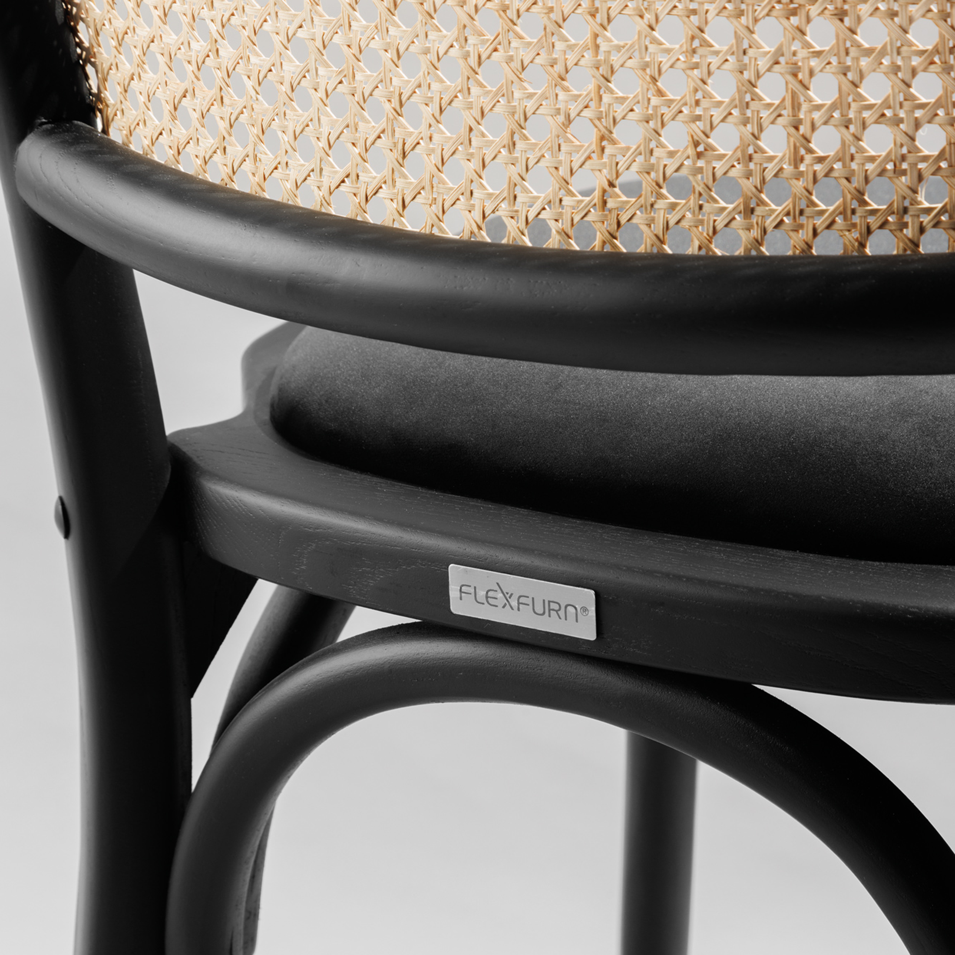Close-up detail of a black wooden frame and woven cane backrest on a chair, featuring the Ronda Stacking Side Chair Seat Pad - Gold Velvet cushion in soft fabric.
