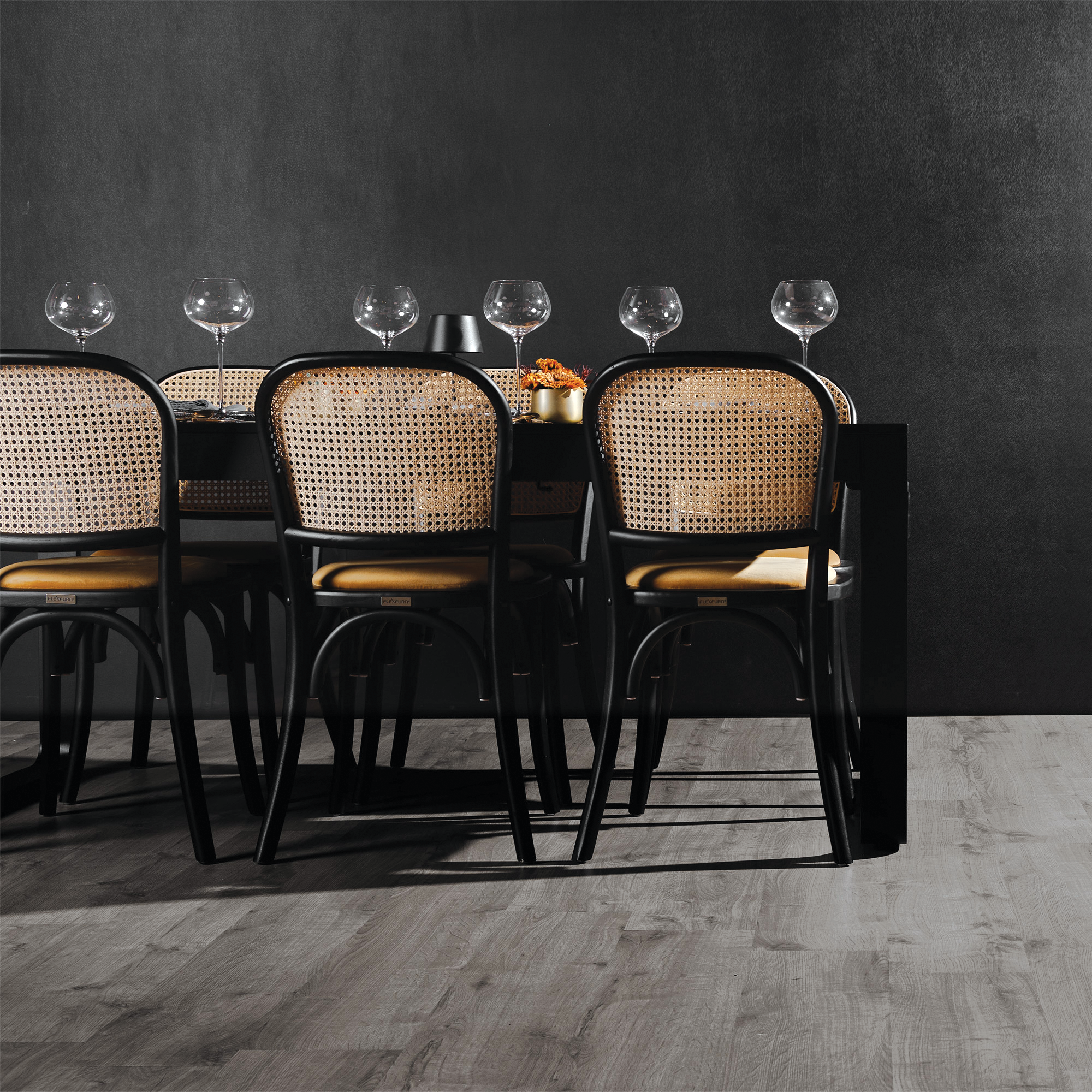 Dining chairs with Ronda Stacking Side Chair Seat Pads - Gold Velvet on a modern wood floor, set against a dark textured wall with wine glasses on a black dining table.