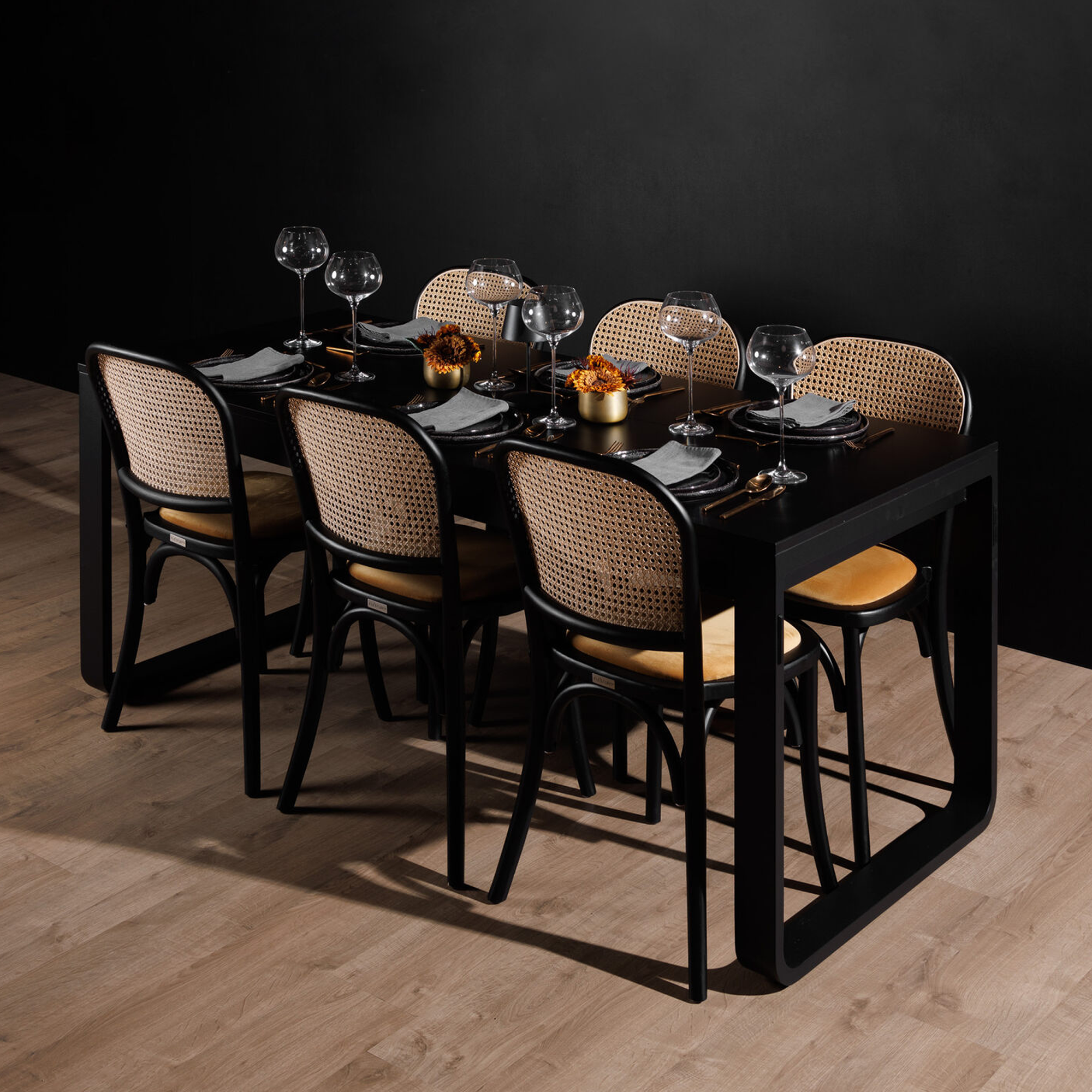 Commercial Interiors Dining table set with black frame chairs featuring woven rattan backs and Ronda Stacking Side Chair Seat Pad - Gold Velvet cushions in a modern, minimalist setting.