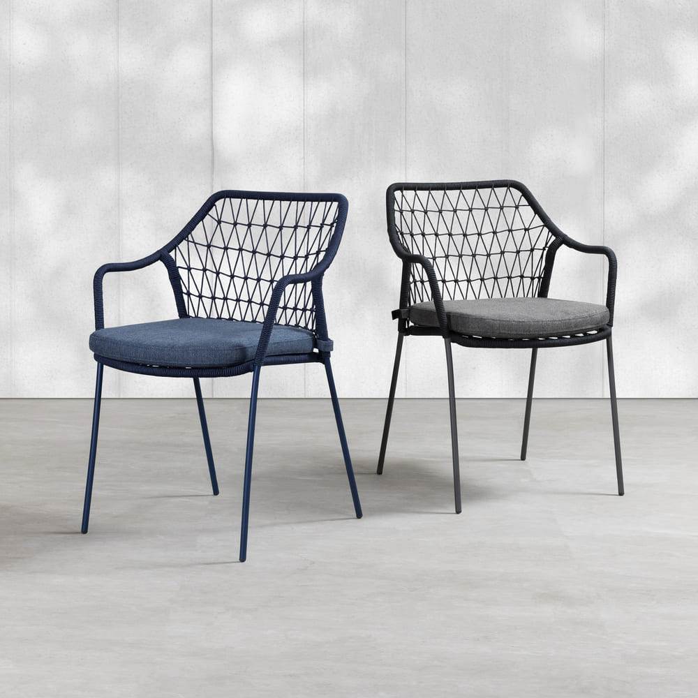 Klein Stacking Arm Chair in Indigo Blue with woven rope backrest, galvanised steel frame and water-repellent cushion for commercial indoor and outdoor hospitality spaces. Two modern chairs with geometric designs on a light gray floor and white wall background.