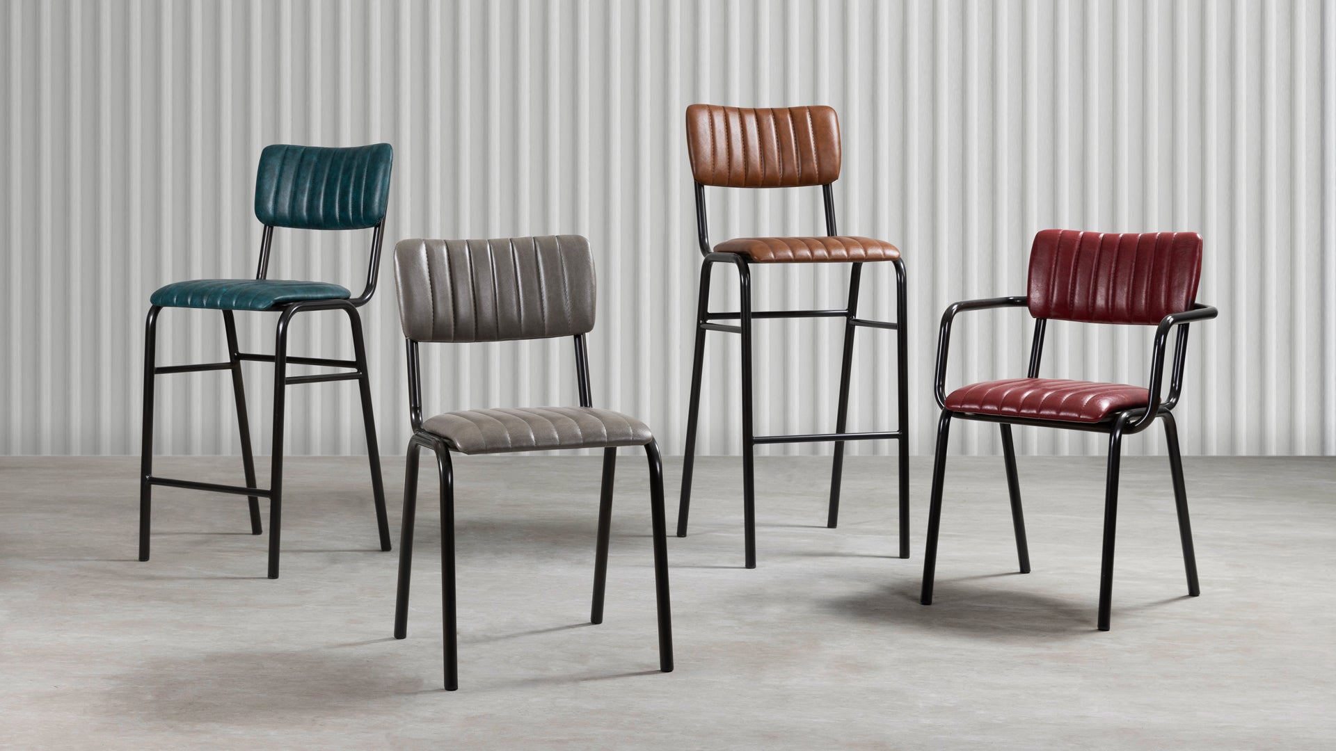Tavo Stacking Mid Height Bar Stool - Ribbed - Lascari Vintage Brown shown alongside three chairs with ribbed upholstery in green, gray, and red, all featuring black metal frames in a modern industrial setting.