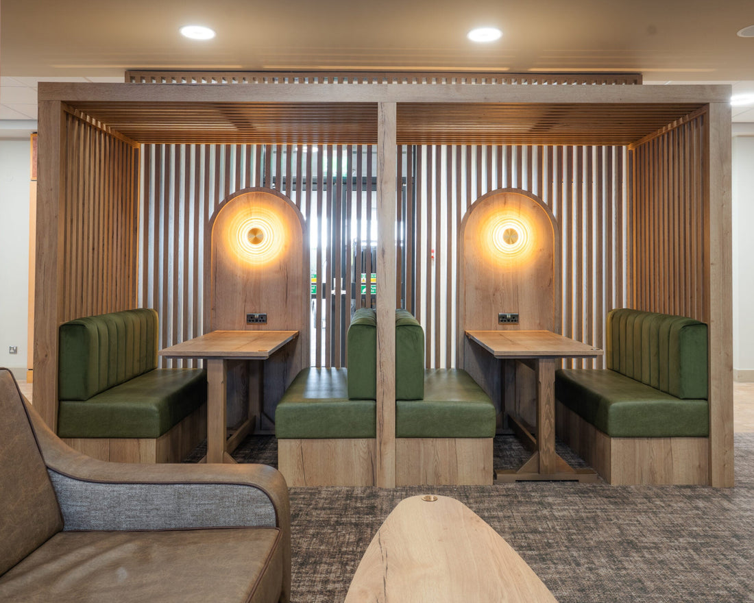 Two wooden booth seating areas with green upholstered benches and wall mounted circular lights