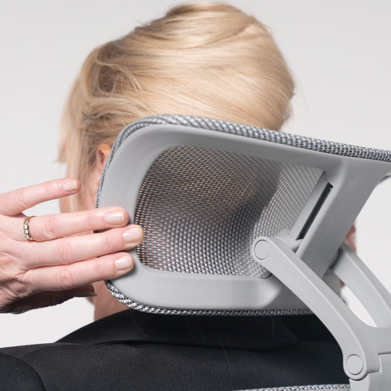 Person holding a gray office chair with mesh backrest against a plain background
